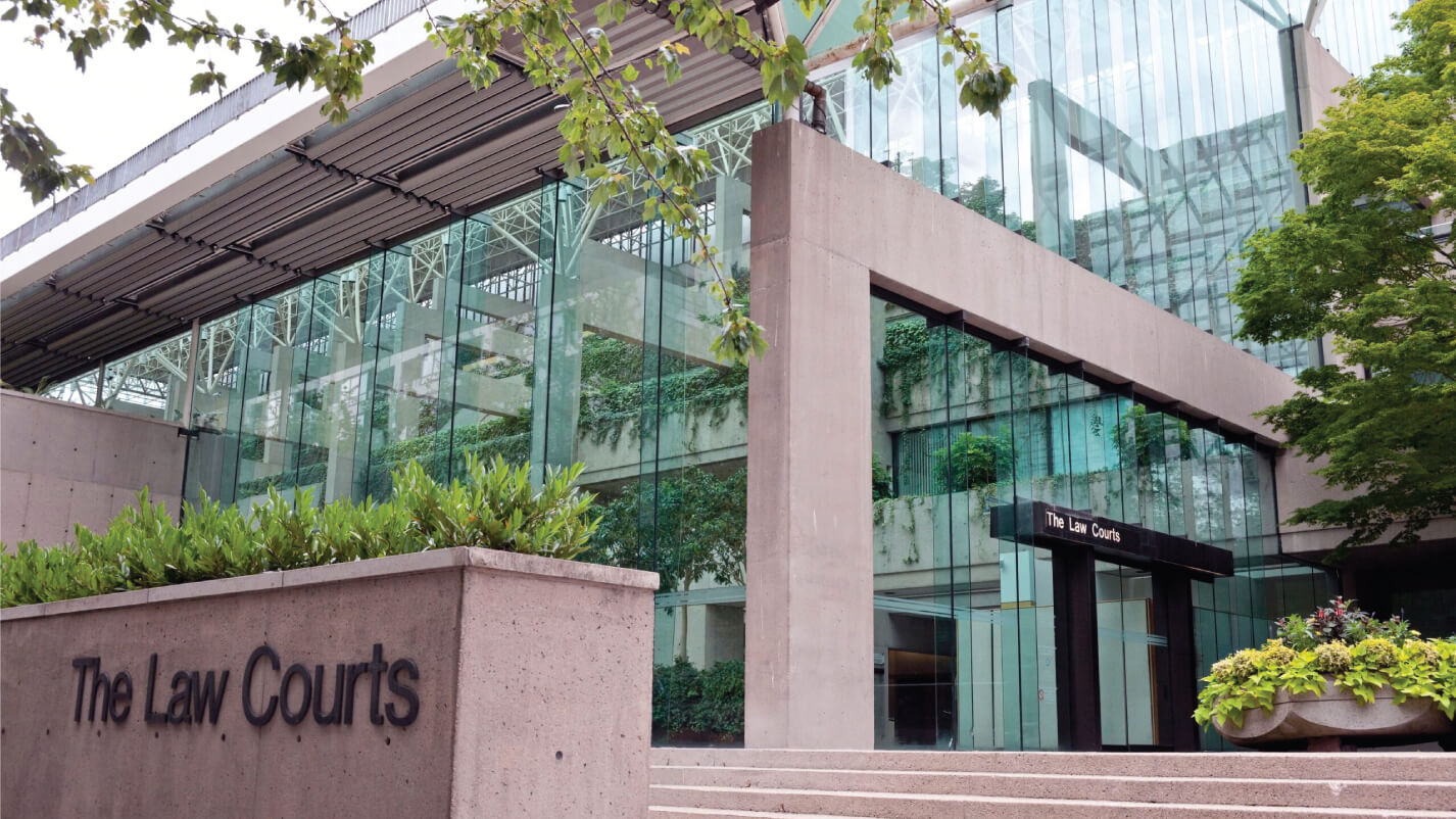 A modern building with large glass windows and greenery, identified as "The Law Courts" by the text on a concrete sign in the foreground. 